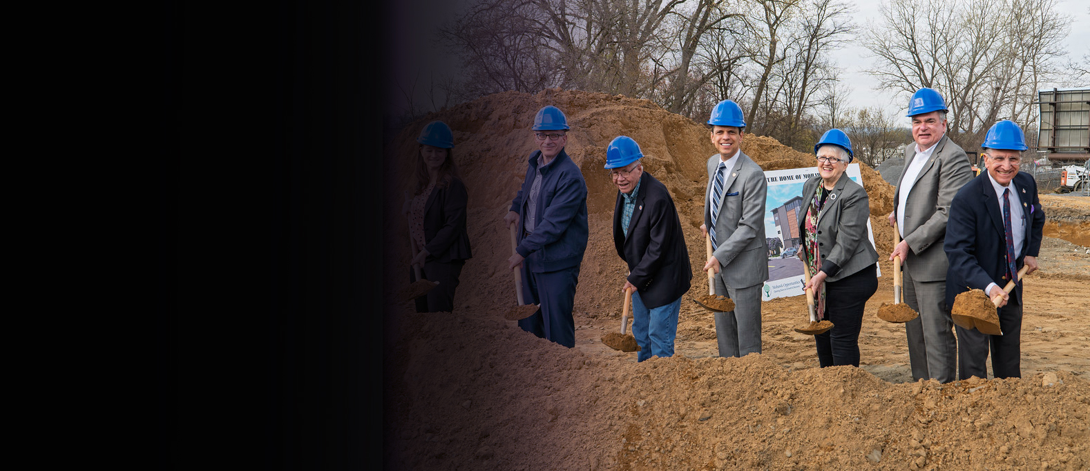Image of construction site with individuals holding shovels of dirt.